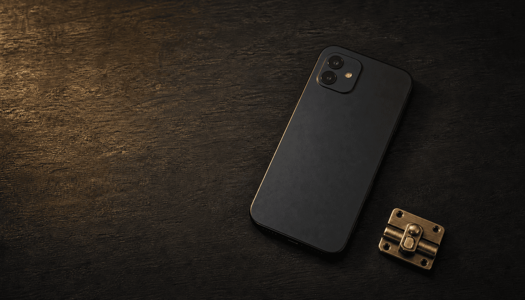 A phone placed face-down beside a closed brass latch on a charcoal table in warm candlelight.