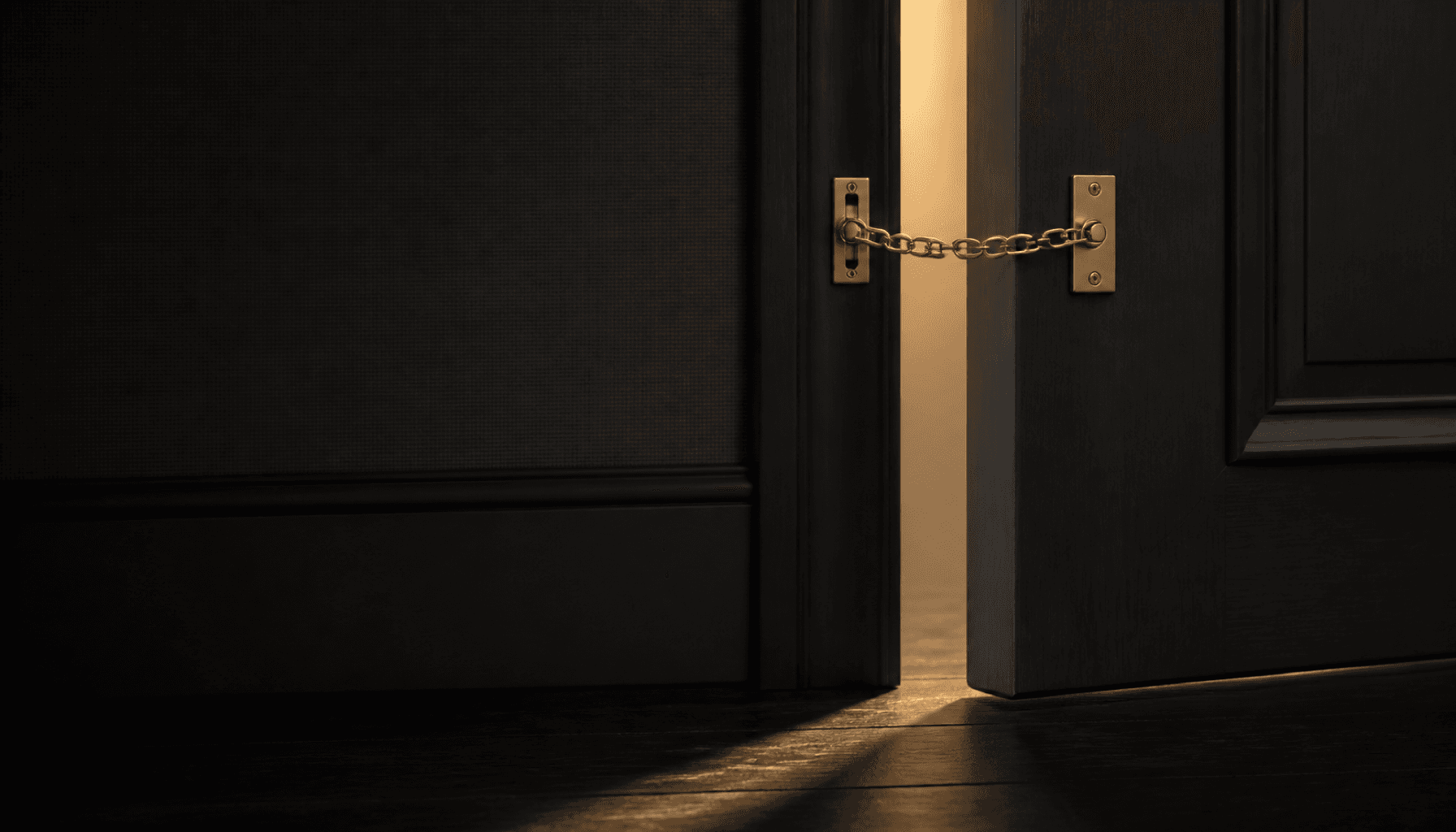 A dark charcoal door open a crack on a brass door chain, with warm light coming through the gap.